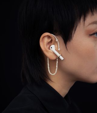 Woman wearing an airpod with pearls dangling round it