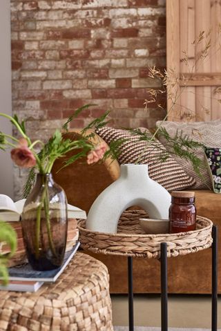 boho style living room with rattan side tables, vase, flowers, couch in background with boho style cushions