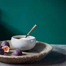 Rustic bowl with figs around it in front of an emerald green painted wall