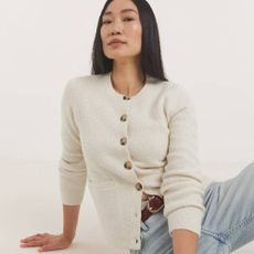 A model wearing a cream knit cardigan and a pair of light blue wash jeans from JD Williams. 