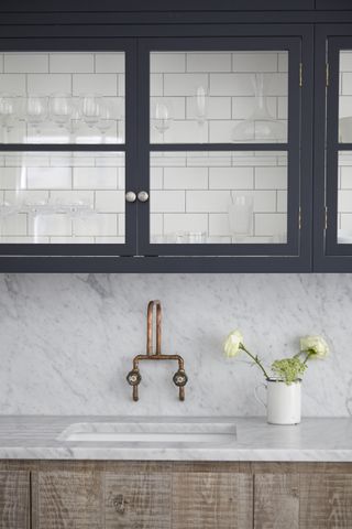 A kitchen with marble countertops and navy cabinets with glass windows