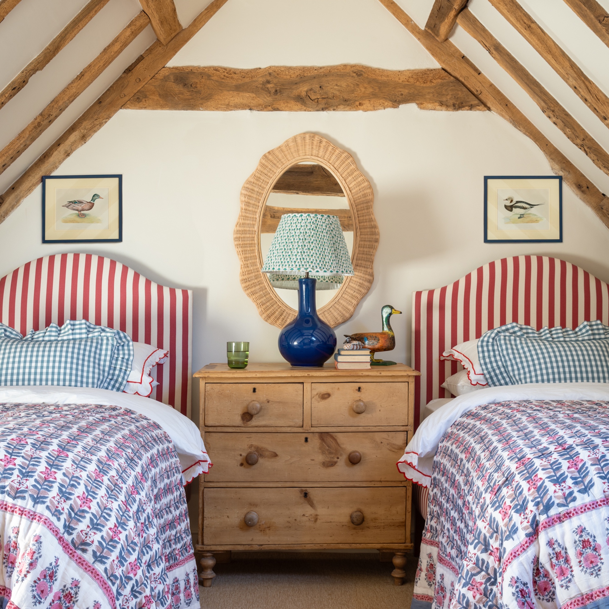 twin bedroom with red and white upholstered bedheads, pine chest of drawers and mirror with wicker frame