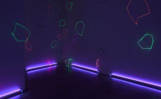 Darkly lit room, neon angle shapes projected onto the walls, neon tube lights lit around the edge of the floor shining up