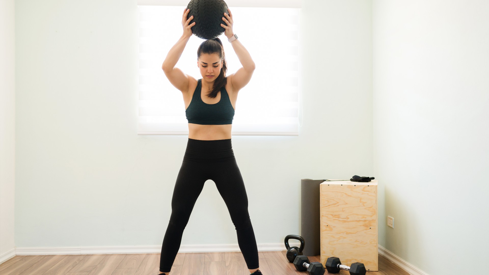 Een vrouw gooit in een homegym een ​​bal over haar hoofd tijdens een medailleschot