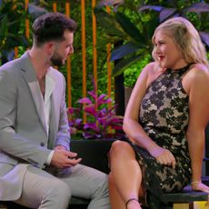 Nick Dorka and Hannah Jiles sit on a bench in front of a foliage wall and candles, on 'Love is Blind' season 7.