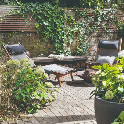 A garden with a folding wooden sun lounger and a matching gardenchair set next to a fire pit
