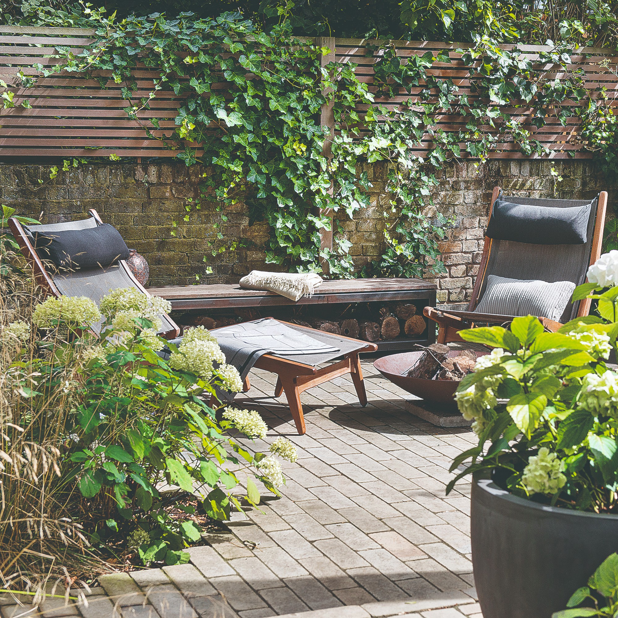 A garden with a folding wooden sun lounger and a matching gardenchair set next to a fire pit
