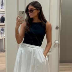 Woman takes photo in mirror wearing black top and white skirt