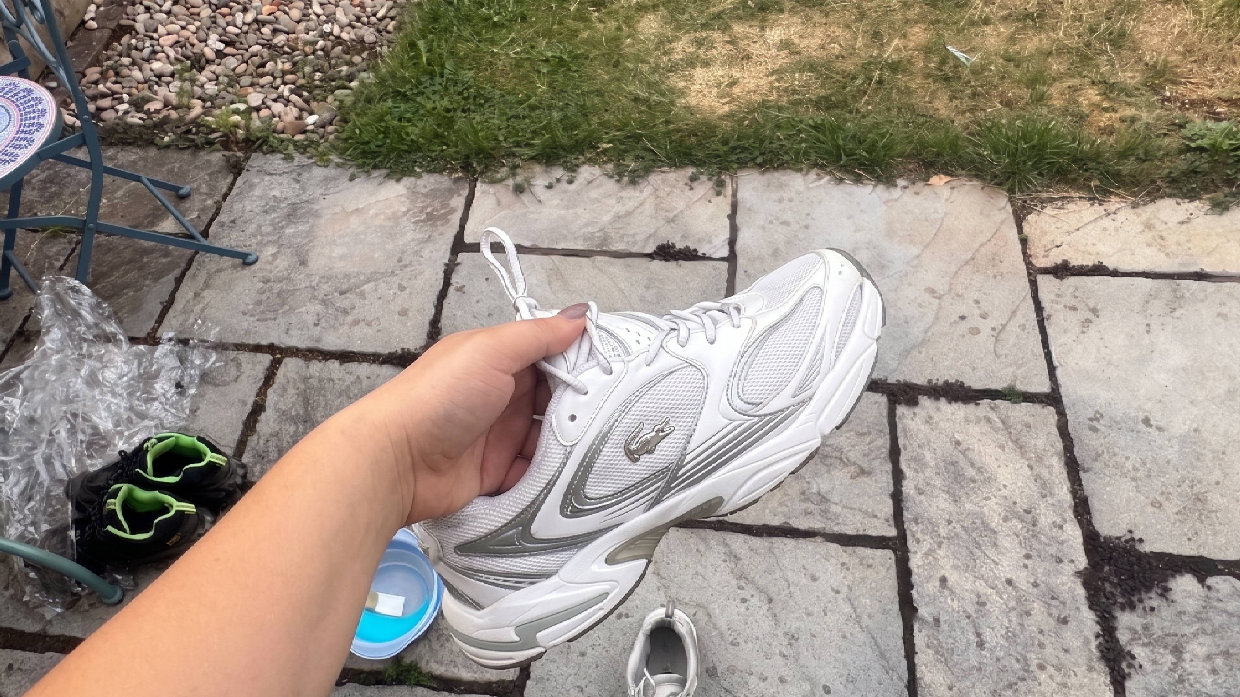 Close-up of a hand holding a freshly cleaned white sneaker, showing the restored fabric and bright white finish.