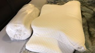 Two Zamat Butterfly Shaped Cervical Memory Foam Pillows, one still rolled and compressed in plastic wrap