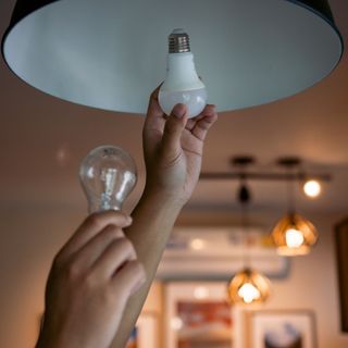 close up of a pair of hands changing a standard lightbulb for a smart lightbulb in a pendant light