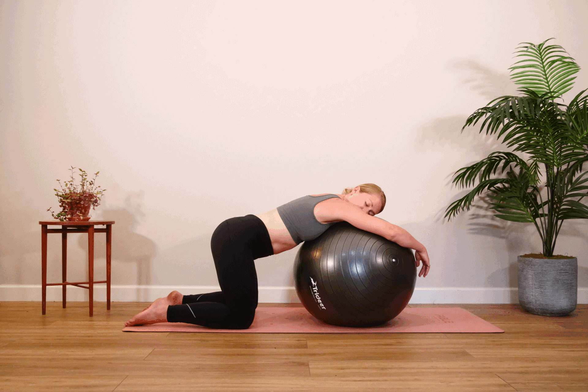 A woman lies on a Swiss ball with her knees on the floor and moves her hips side to side