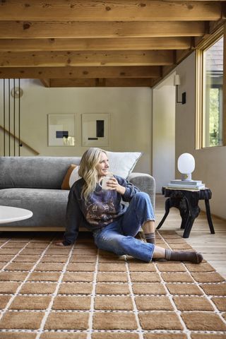 emily henderson sitting on brown check rug with gray sofa and timber ceiling