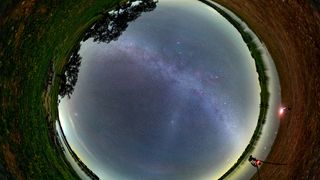 all-sky circular image showing the milky way going across the center and trees and a lake around the perimeter of the circle