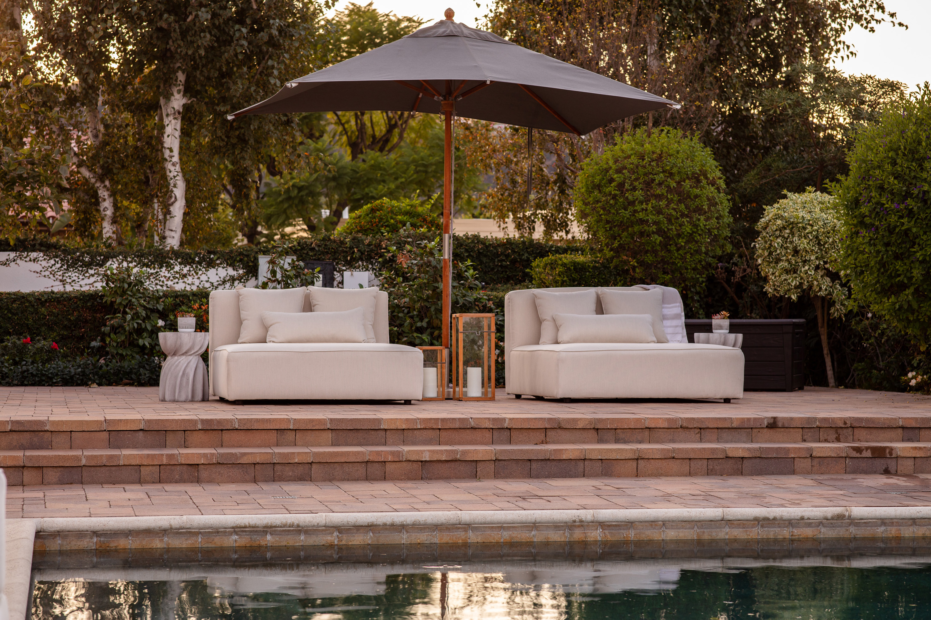 pool landscaping ideas: brick steps leading up from a pool to a raised patio with loungers and a parasol