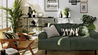 Green sofa in a modern boho living room with black display shelves and a rattan chair from Habitat