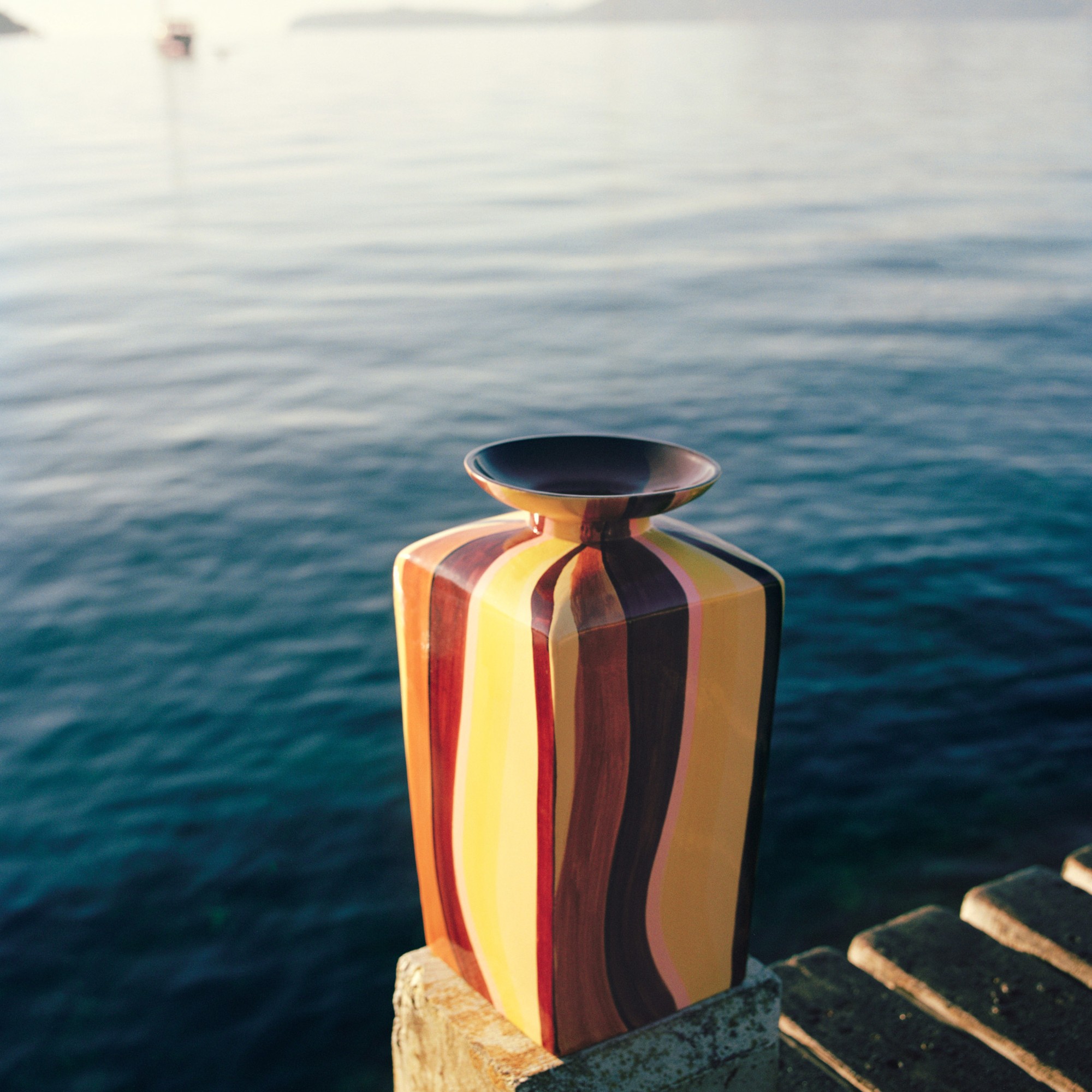 A striped brown and yellow vase from the Zara Home x Collagerie collection against the backdrop of sea