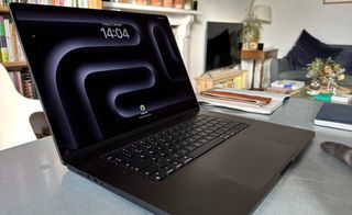 A Space Black Apple MacBook Pro 16-inch M3, one of the best MacBooks for programming, sitting on a grey/blue table