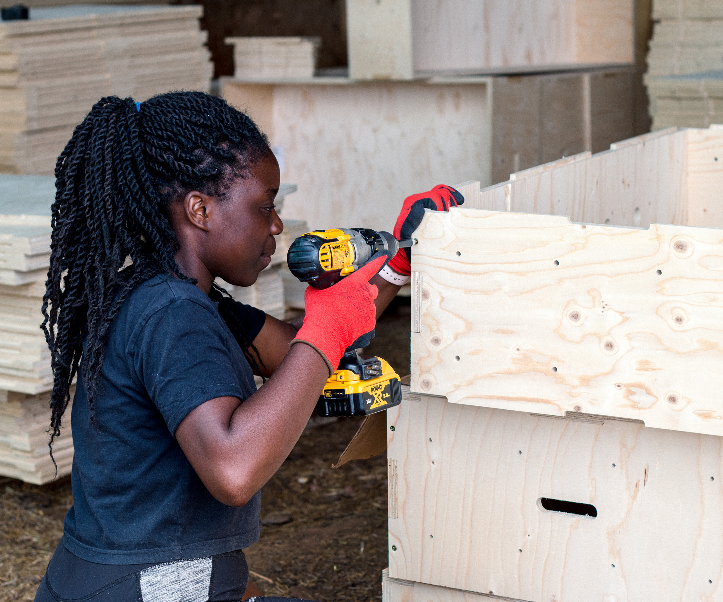 Young trainee construction worker uses a drill to put together modular timber pieces for a self-build project