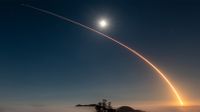 A rocket launch carves an orange arc into a dark night sky in this long-exposure photo.