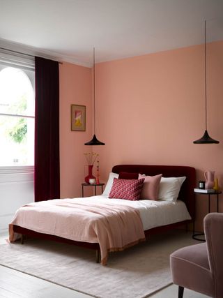 coral and white bedroom with magenta velvet bed and matching drapes, black pendants, white floor, pink accessories