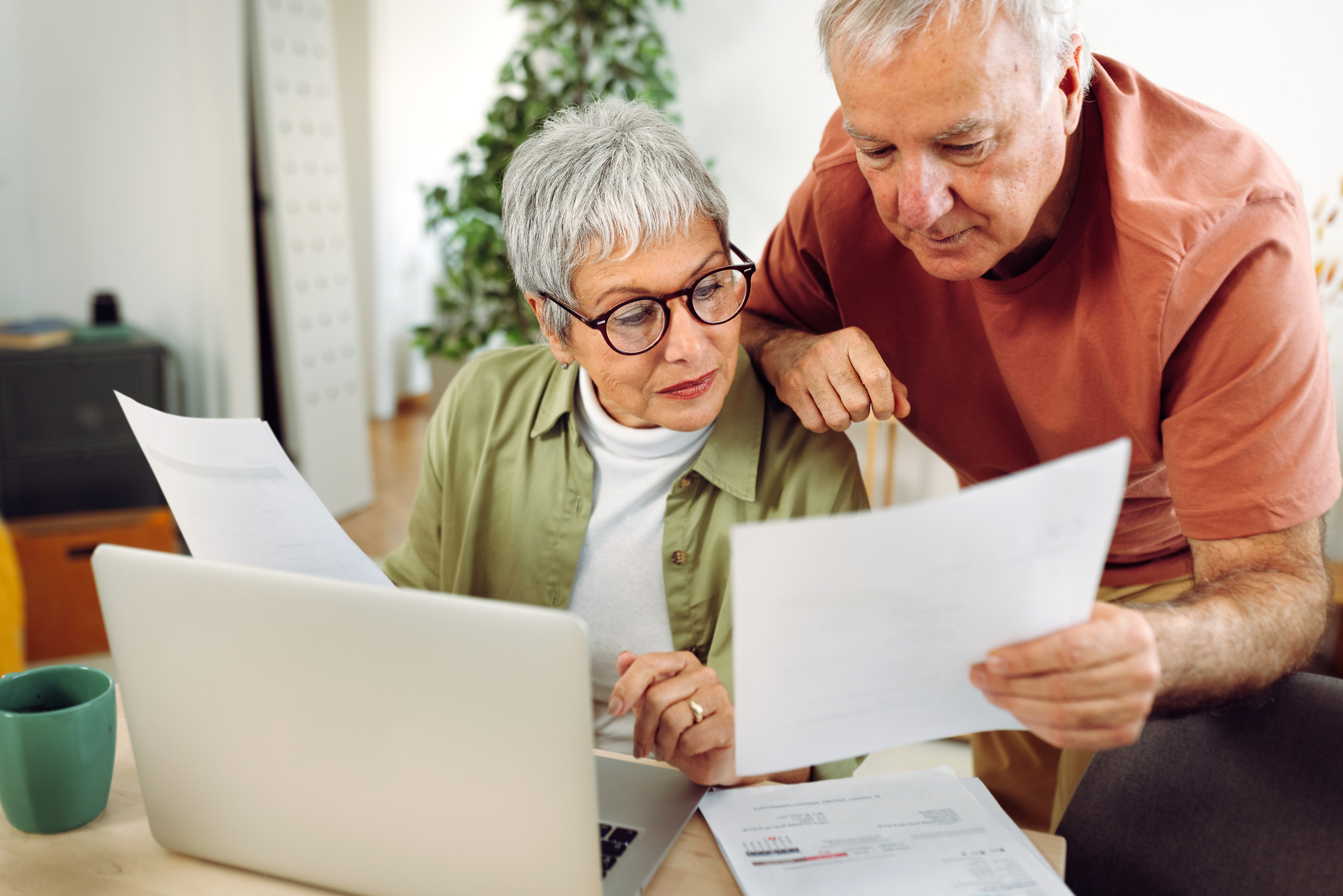 A senior couple reviews paperwork together at their dining table.