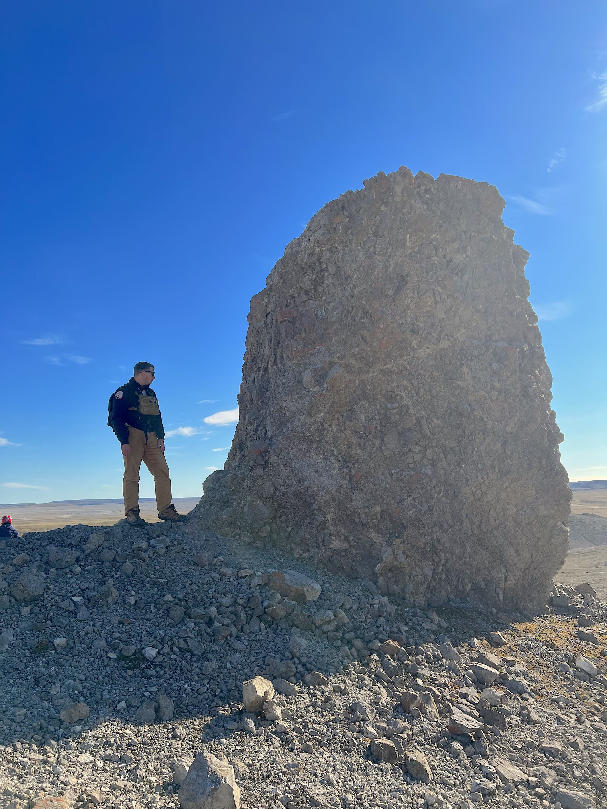A man stands next to a large boulder