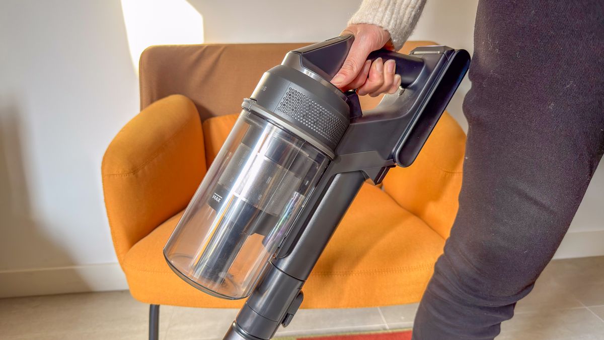 A person holding the Samsung Jet 95S in front of a chair
