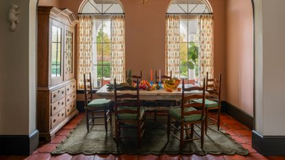 a sunny dining room in a home in Miami with large arched patio doors, wallpapered walls, terracotta floors, a green scalloped rug and antique furniture