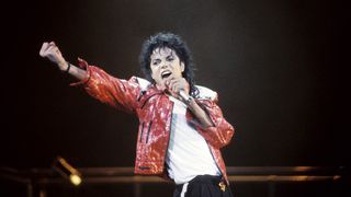 A closeup of Michael Jackson with a red jacket, singing live on stage