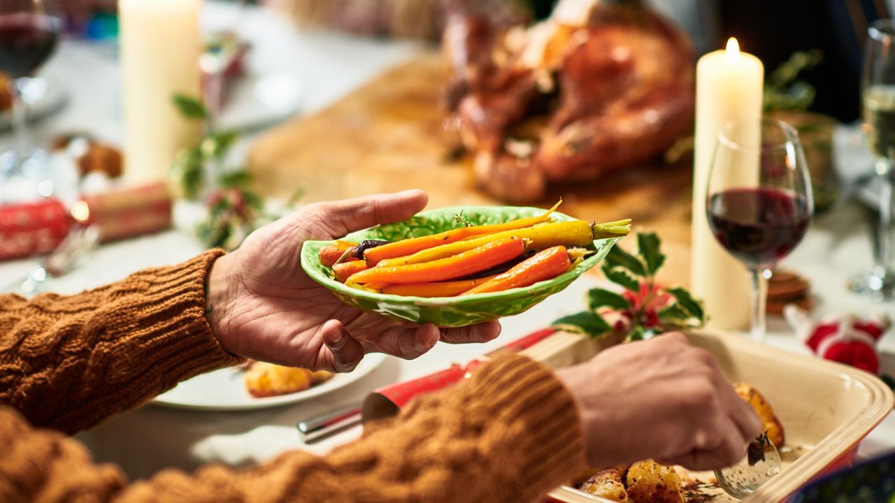 table with vegetables and serving dish of roasted carrots, roast turkey resting in background, lit candles and red wine