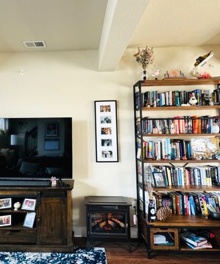 A white living room with a TV on a TV stand, a black freestanding fireplace, and a tall bookshelf