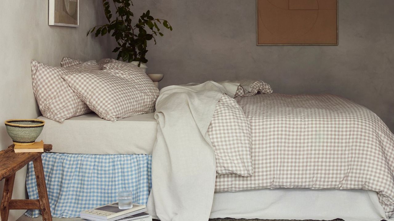 Side view of oatmeal, white, and blue gingham prints on a bed against a beige wall. 