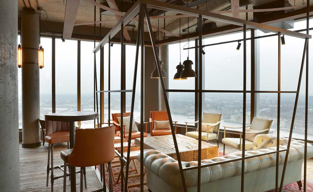 A restaurant sitting area with a white sofa, various sized chairs, a natural wood finished table, large windows and pendant lights.