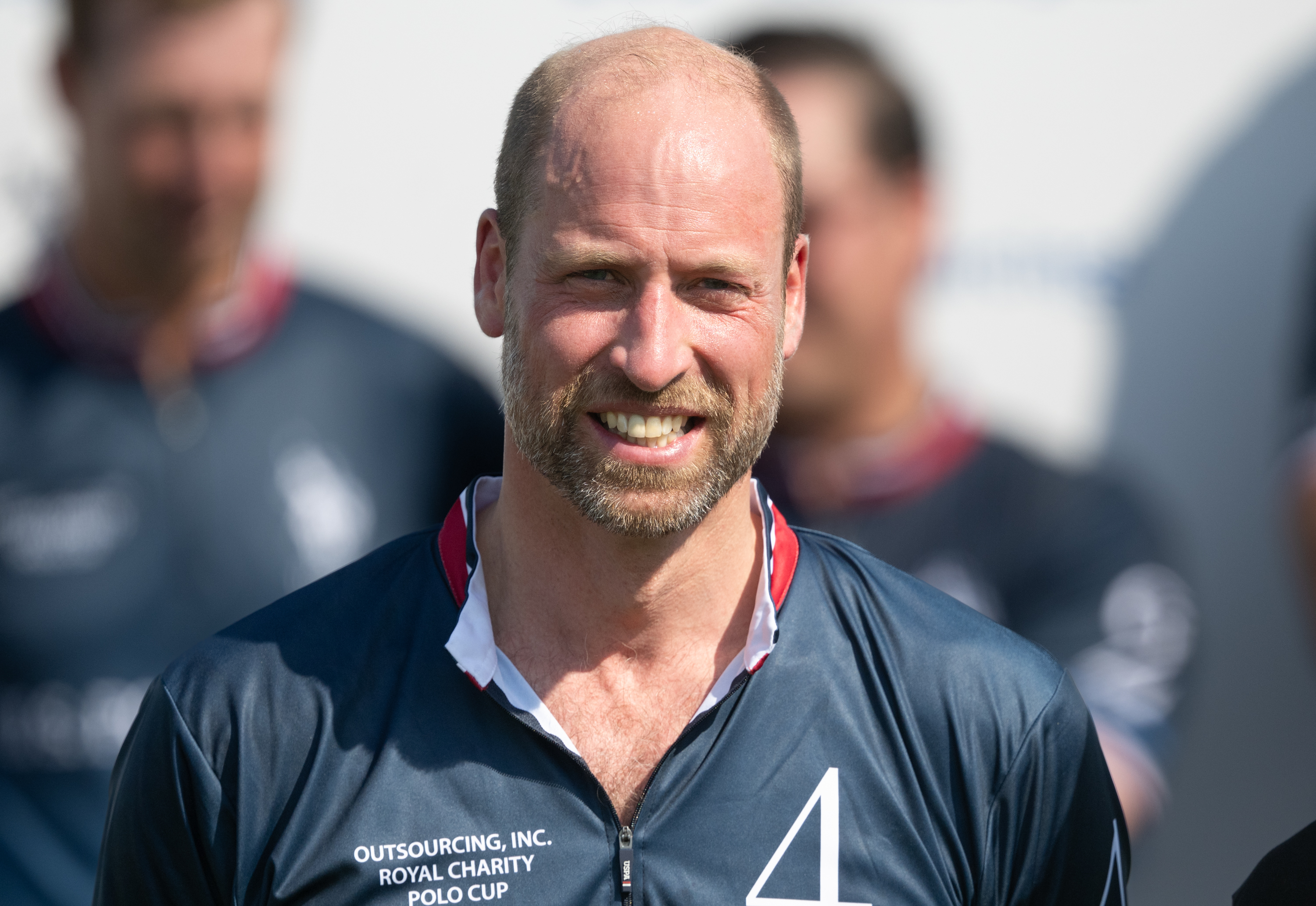 Prince William wearing a blue polo top and smiling