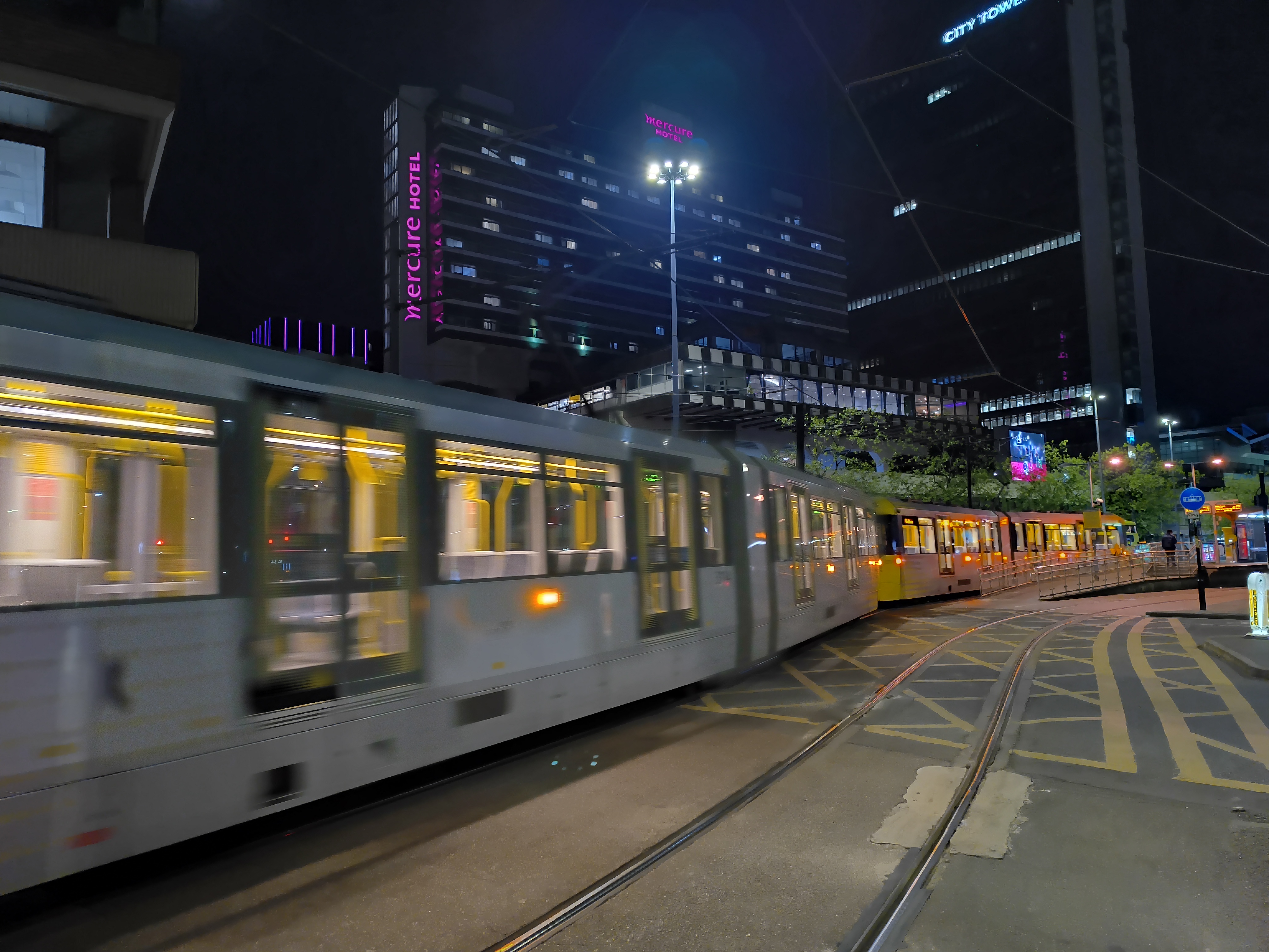 A light rail tram passing through a city center at night with illuminated carriages.