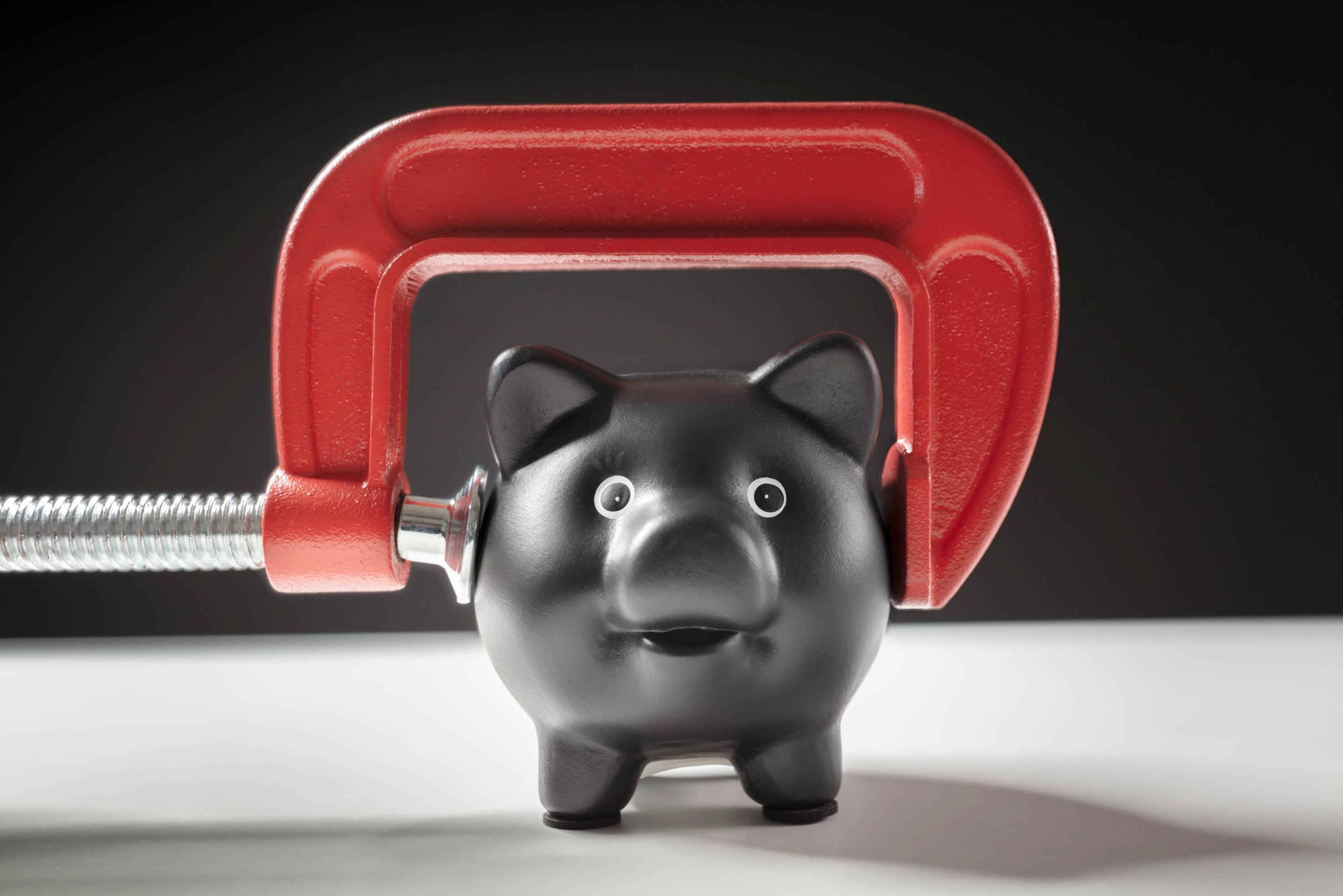 A black piggy bank is being clamped by a vice. 
