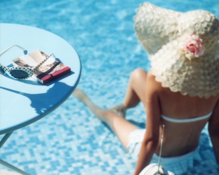 An example of pool party ideas showing a woman sat by a pool with a large sun hat next to a table