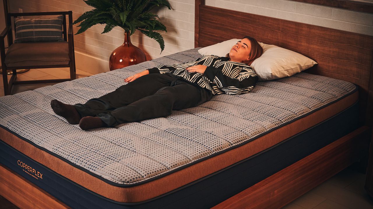 Our mattress tester in white and black silk pyjamas laying on her back on the Brooklyn Bedding Copperflex Memory Foam Mattress on wooden bed frame in sleep studio.