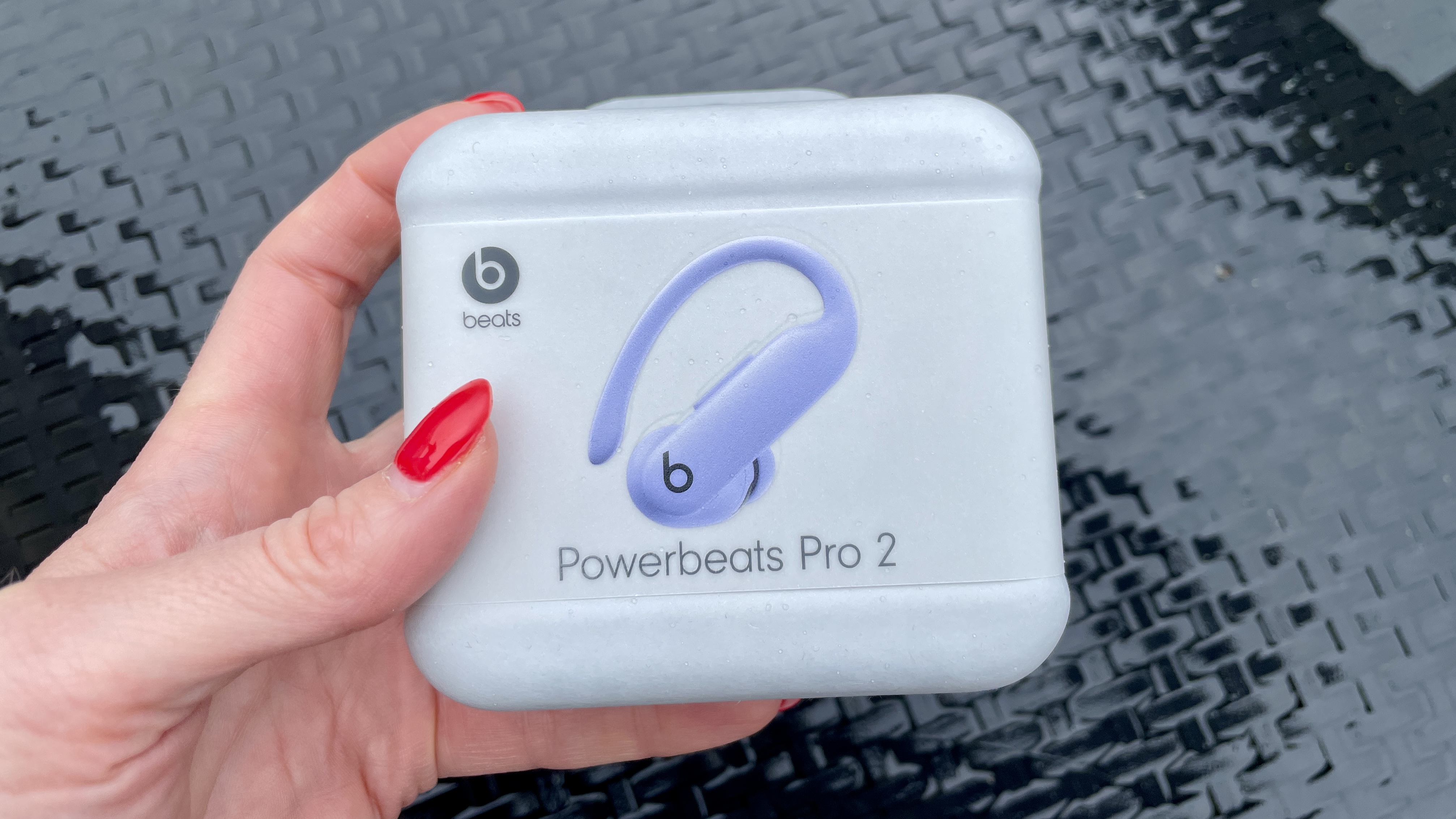 Beats Powerbeats Pro 2 in packaging, held outside above a black table