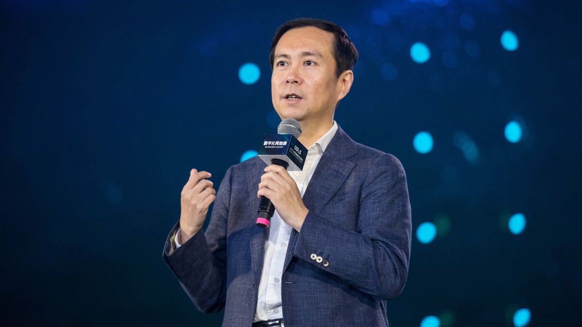 Former Alibaba CEO Daniel Zhang holding a microphone on stage. Shot on a telephoto lens, with blue lights in the background against a dark backdrop.