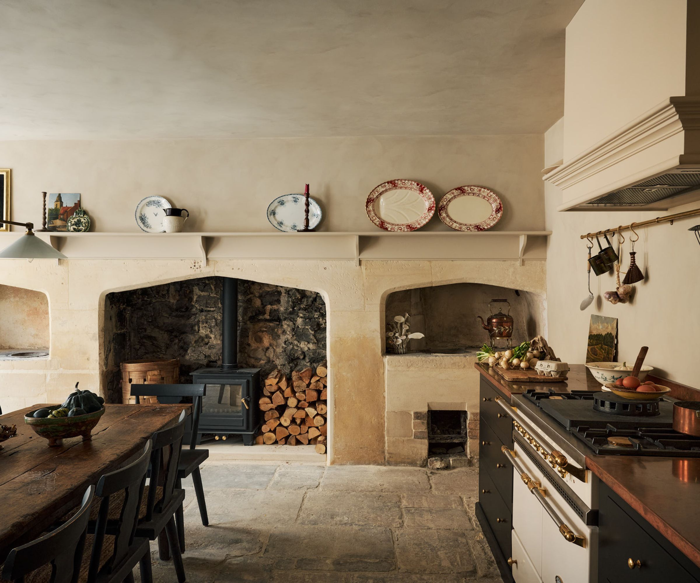 A traditional country kitchen with plaster walls, an original fireplace, dark cabinets, and wooden countertops