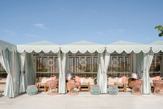 Blue striped cabanas by a pool with pastel pink outdoor furniture