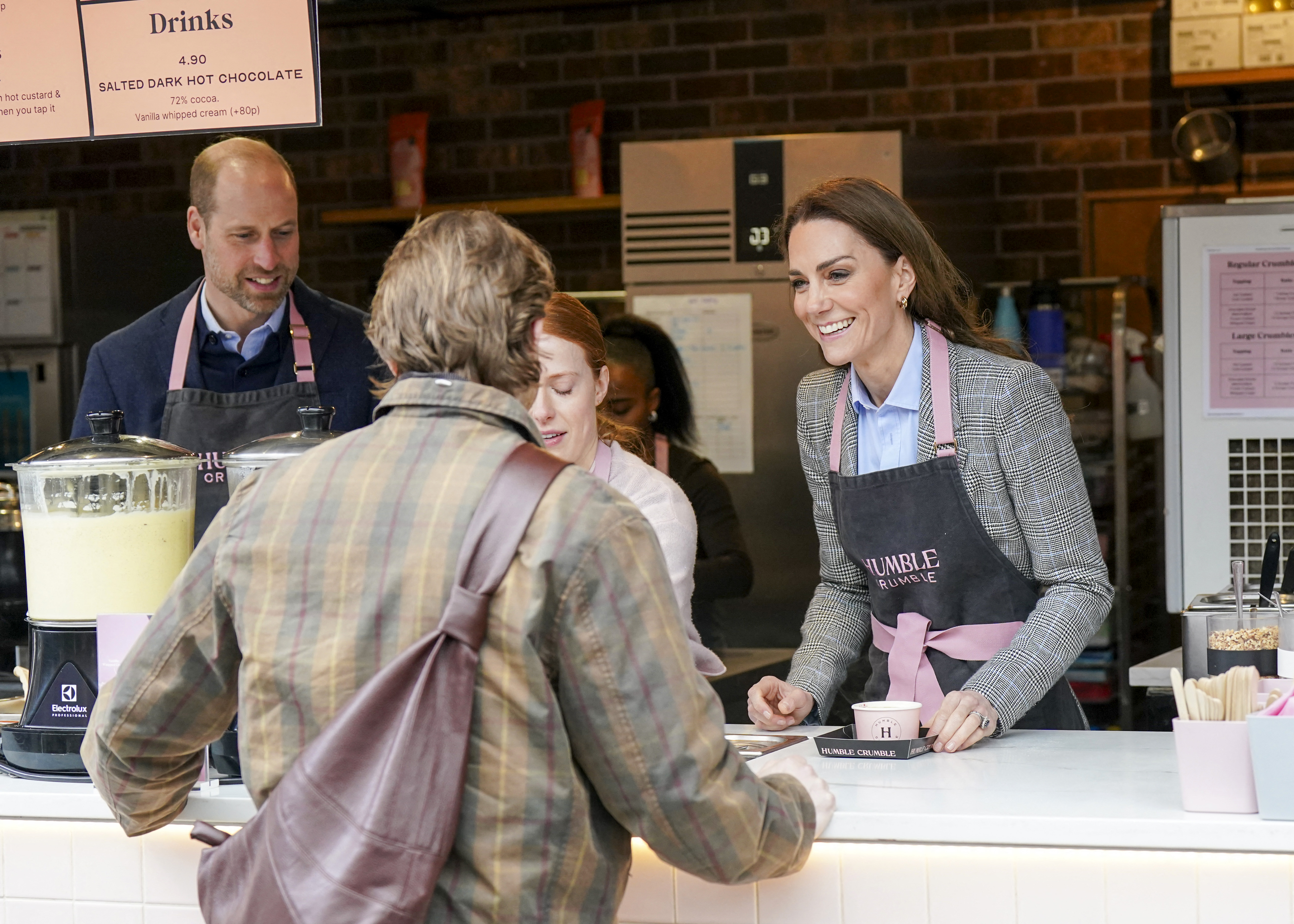 Prince William and Princess Kate wearing aprons serving coffee to customers