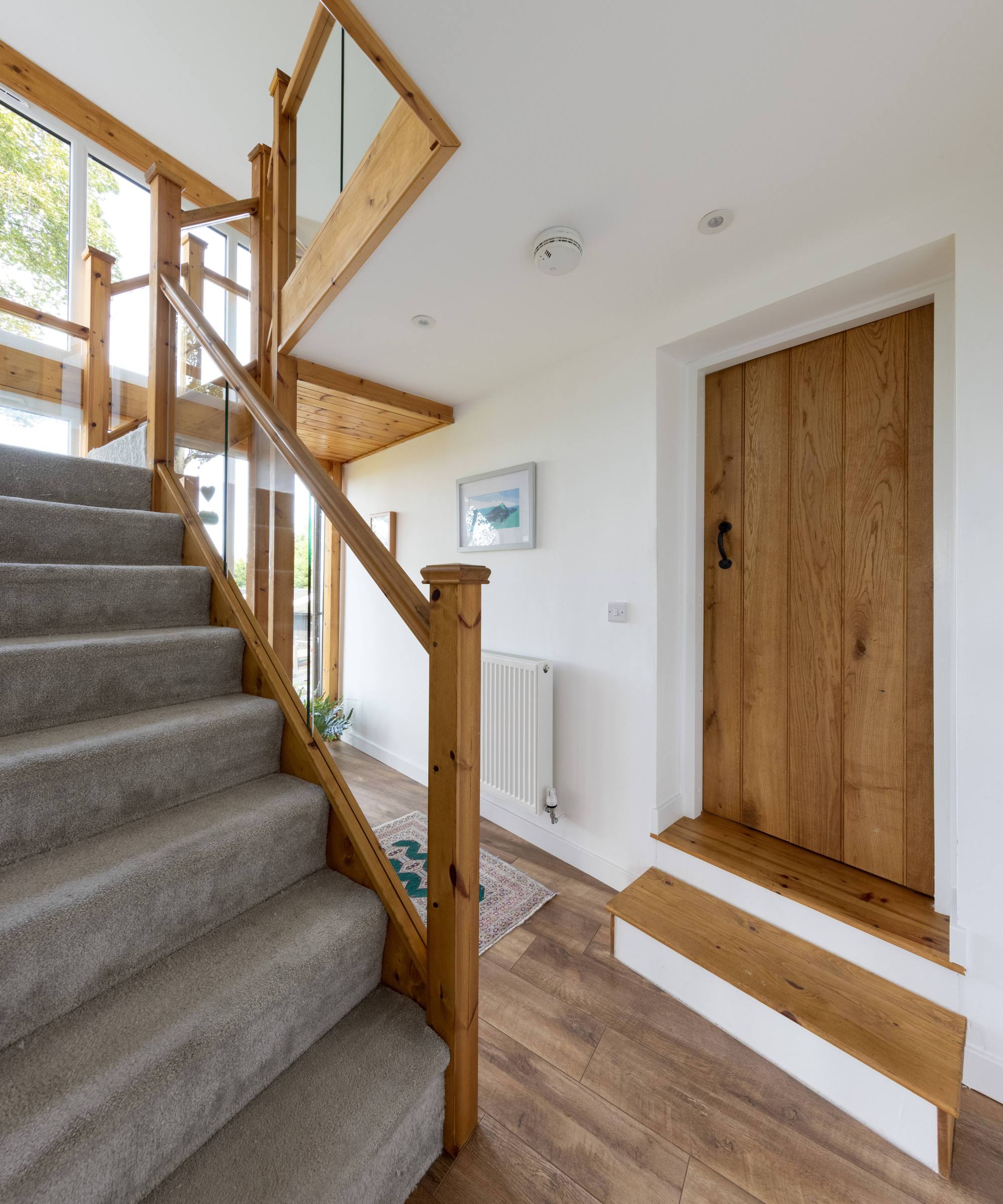 Wooden wide-stepped and grey carpeted staircase with glass siding