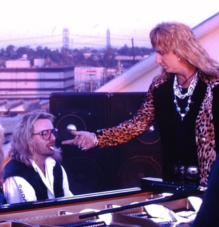 Great White Manager Alan Niven sits at a piano smoking with singer Jack Russell