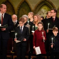 Prince William wears a suit and looks at his family, Prince George, Princess Charlotte, Prince Louis, and wife Kate Middleton who wears a white suit