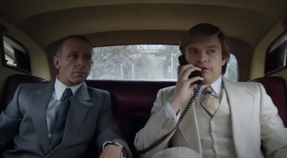 Sebastian Stan on the phone in the back of a car as Donald Trump with Jeremy Strong's Roy Cohn on his right in 2024 movie The Apprentice