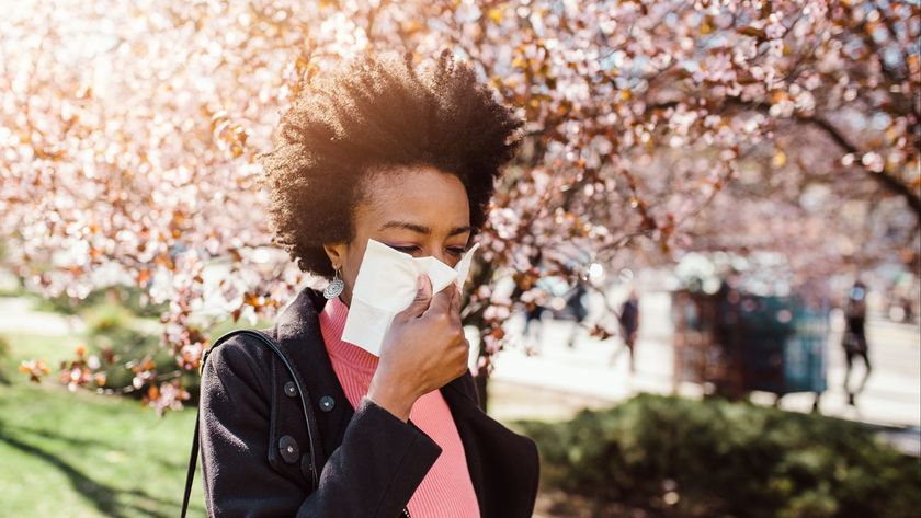 black woman walking through a city park with blooming cherry trees in the background as she blows her nose into a tissue