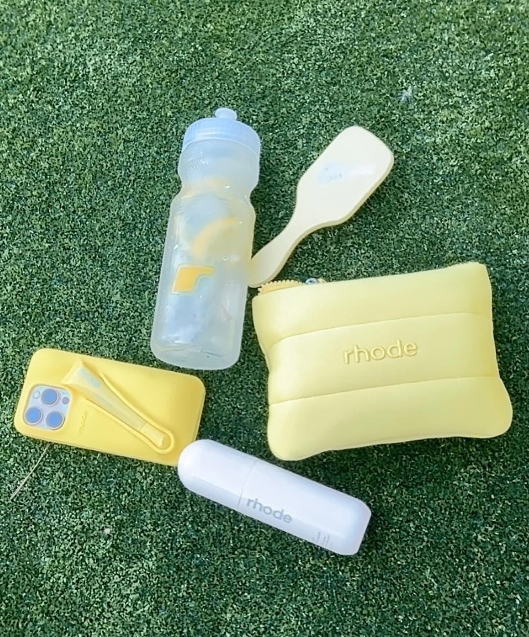 A photo of a phone case, water bottle, hair brush, and rhode makeup case.